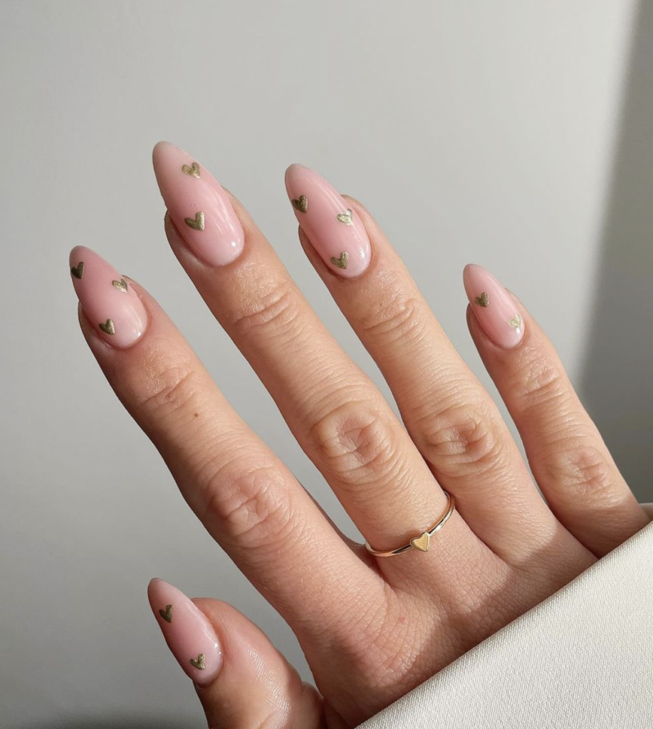 Close-up of nails with a soft pink base and gold heart accents.